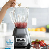 Hand adding fiber blend supplement powder to blender with berries on kitchen counter