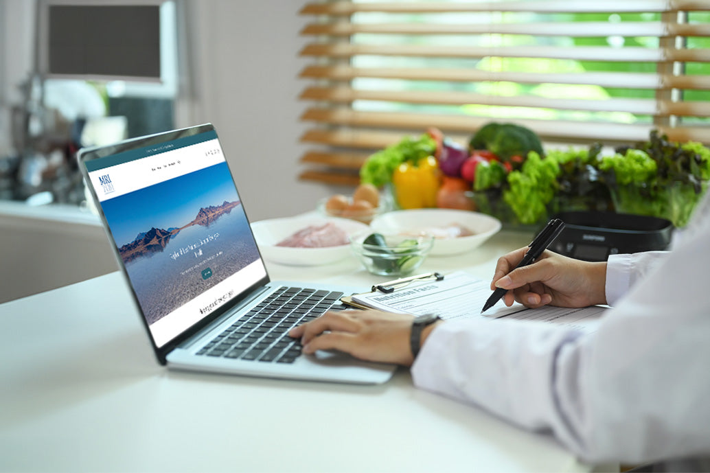 Person using a laptop with a health-related website on a kitchen counter with vegetables.