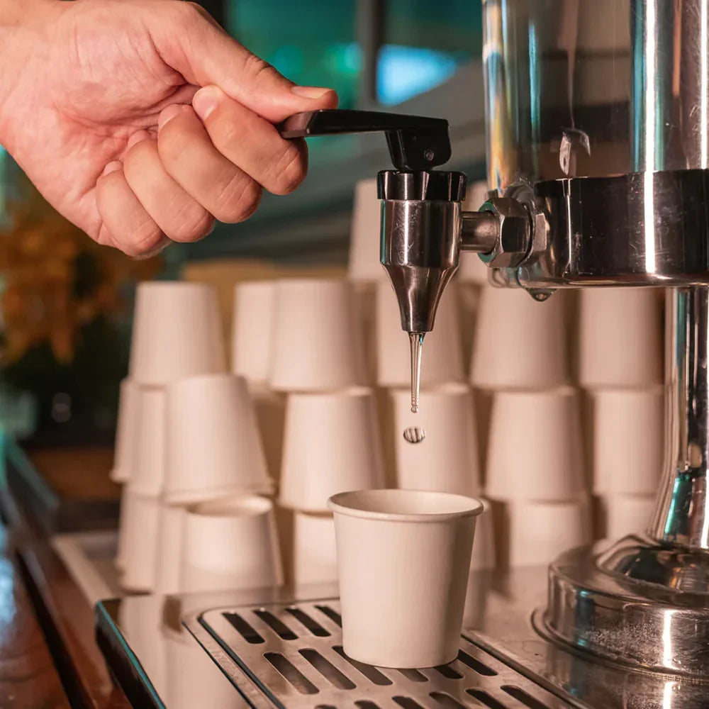 Hand operating a coffee machine with a paper cup receiving a shot of espresso.