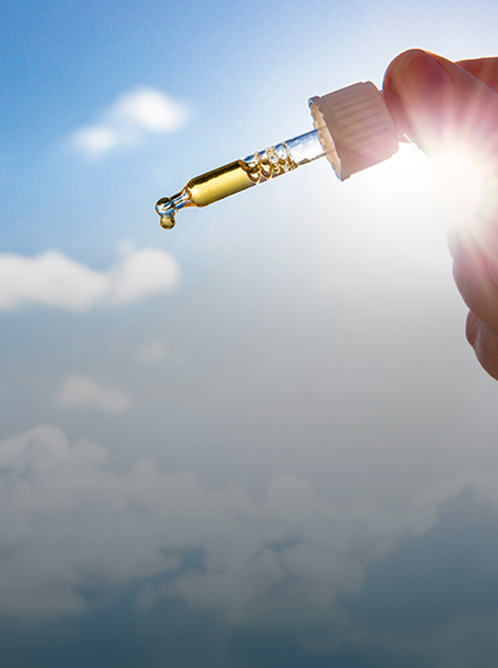 Hand holding a dropper with a clear liquid against a blue sky.