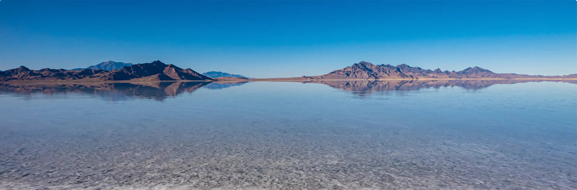 Panoramic view of a salt lake with mountains in the distance under a clear blue sky.