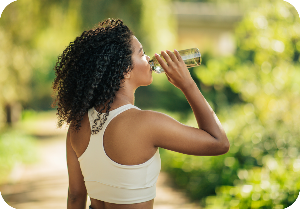 Woman drinking from a water bottle outdoors with greenery in the background
