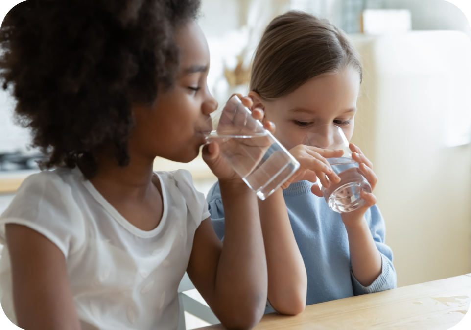 Two children drinking water from bottles indoors.