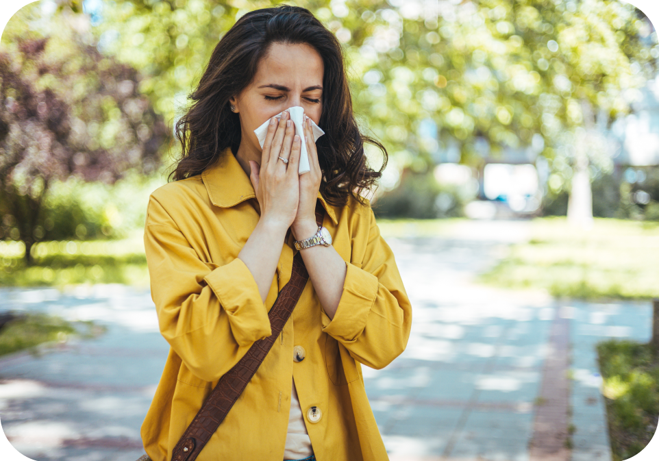 Woman in a yellow coat blowing her nose outdoors