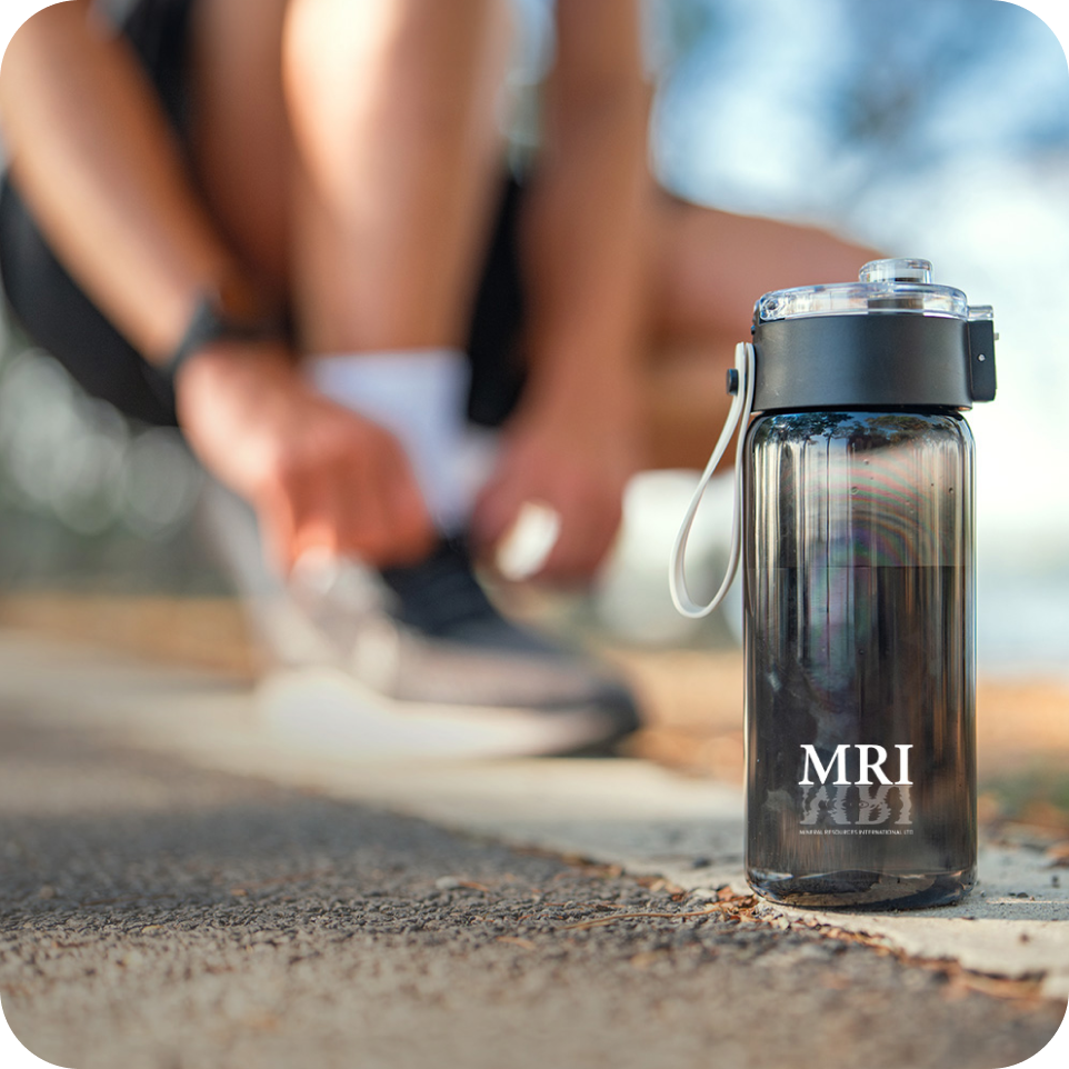 Person tying shoelaces with a clear water bottle featuring 'MRI' branding on a blurred outdoor background.