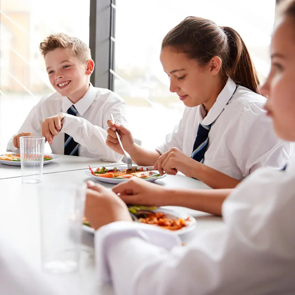 Children in school uniforms eating lunch together at a table.