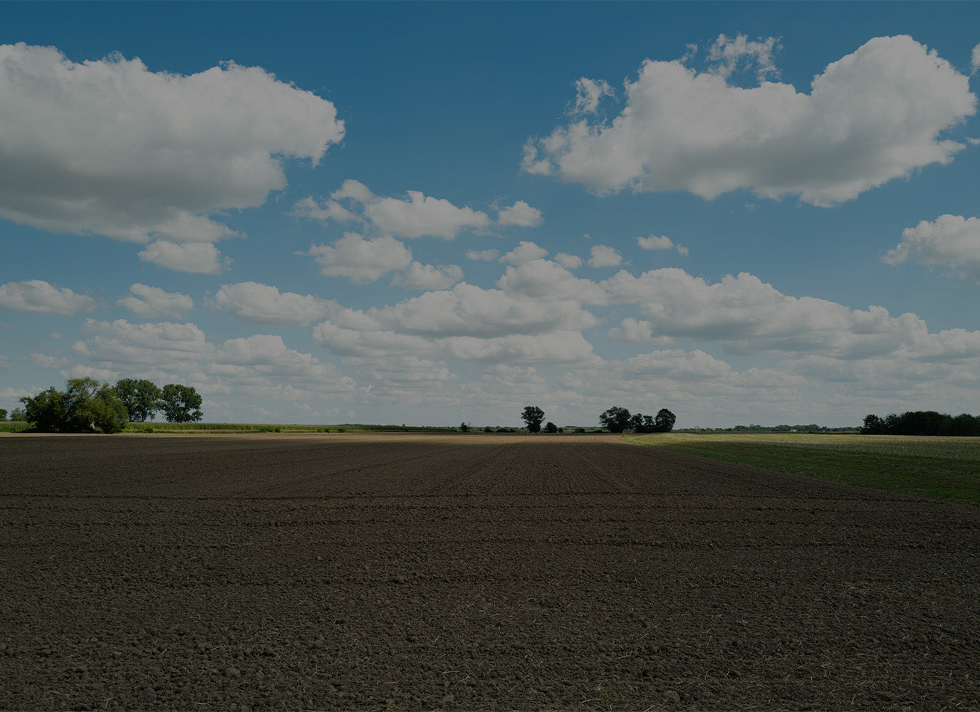 Plowed field under a blue sky with scattered clouds