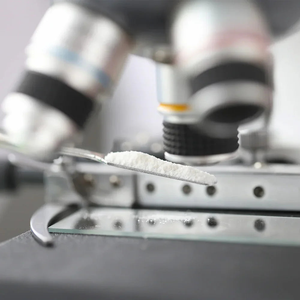 Close-up of a spoon with white powder in front of a microscope