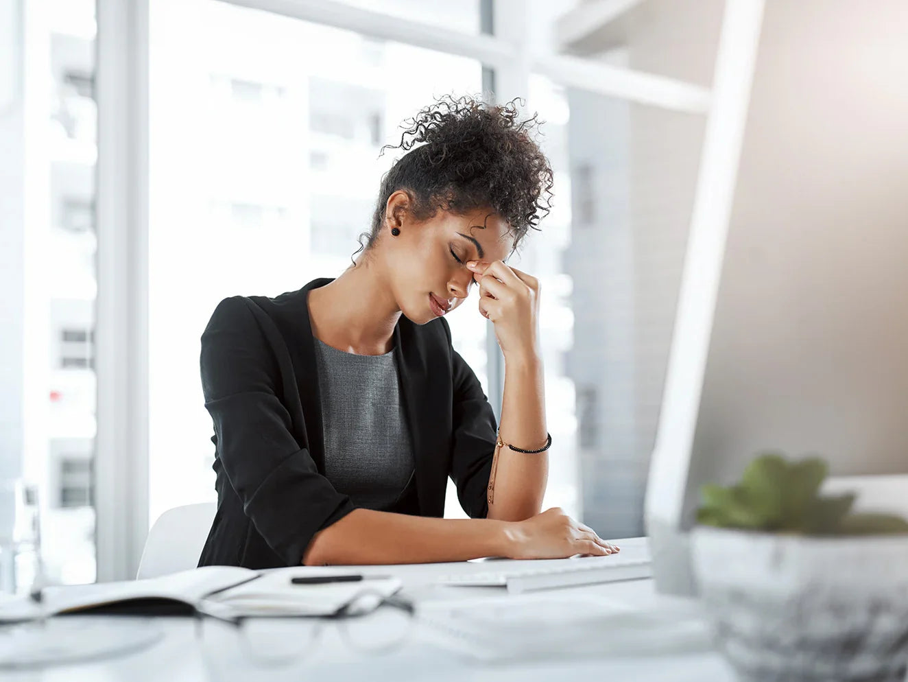 Woman sitting at a desk with her head in her hands, possibly feeling stressed or overwhelmed.