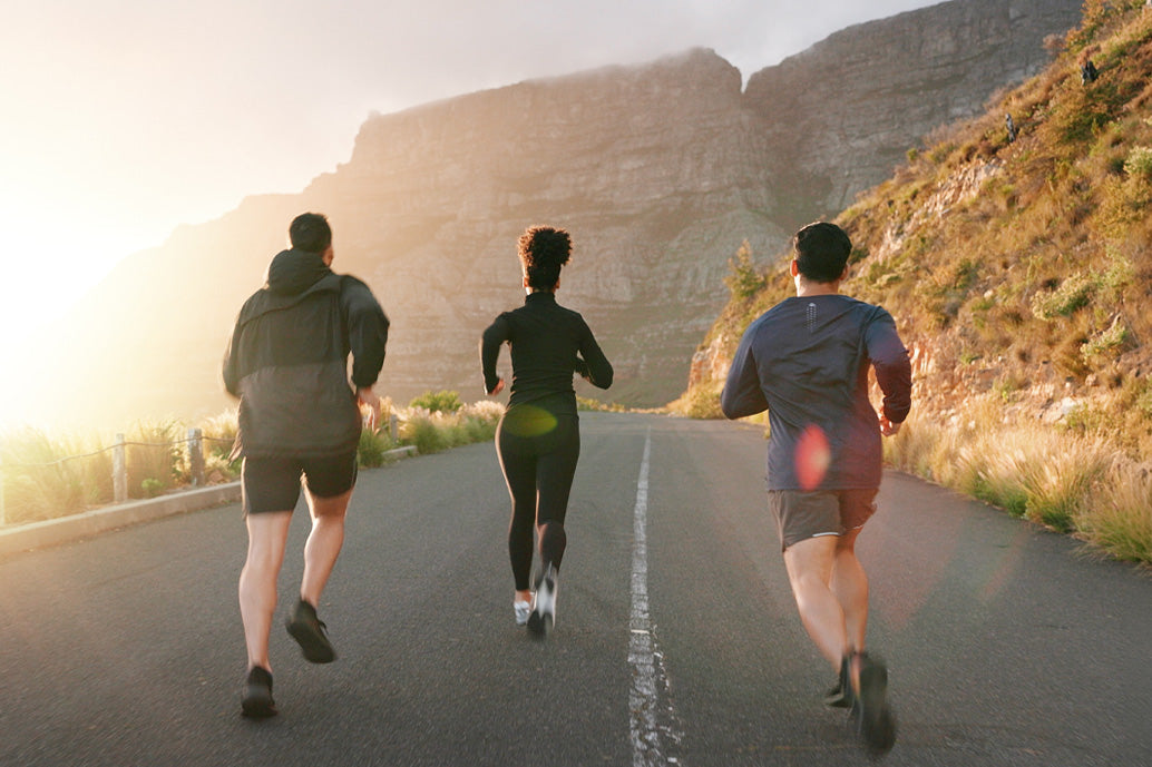 Three people running on a road with mountains in the background