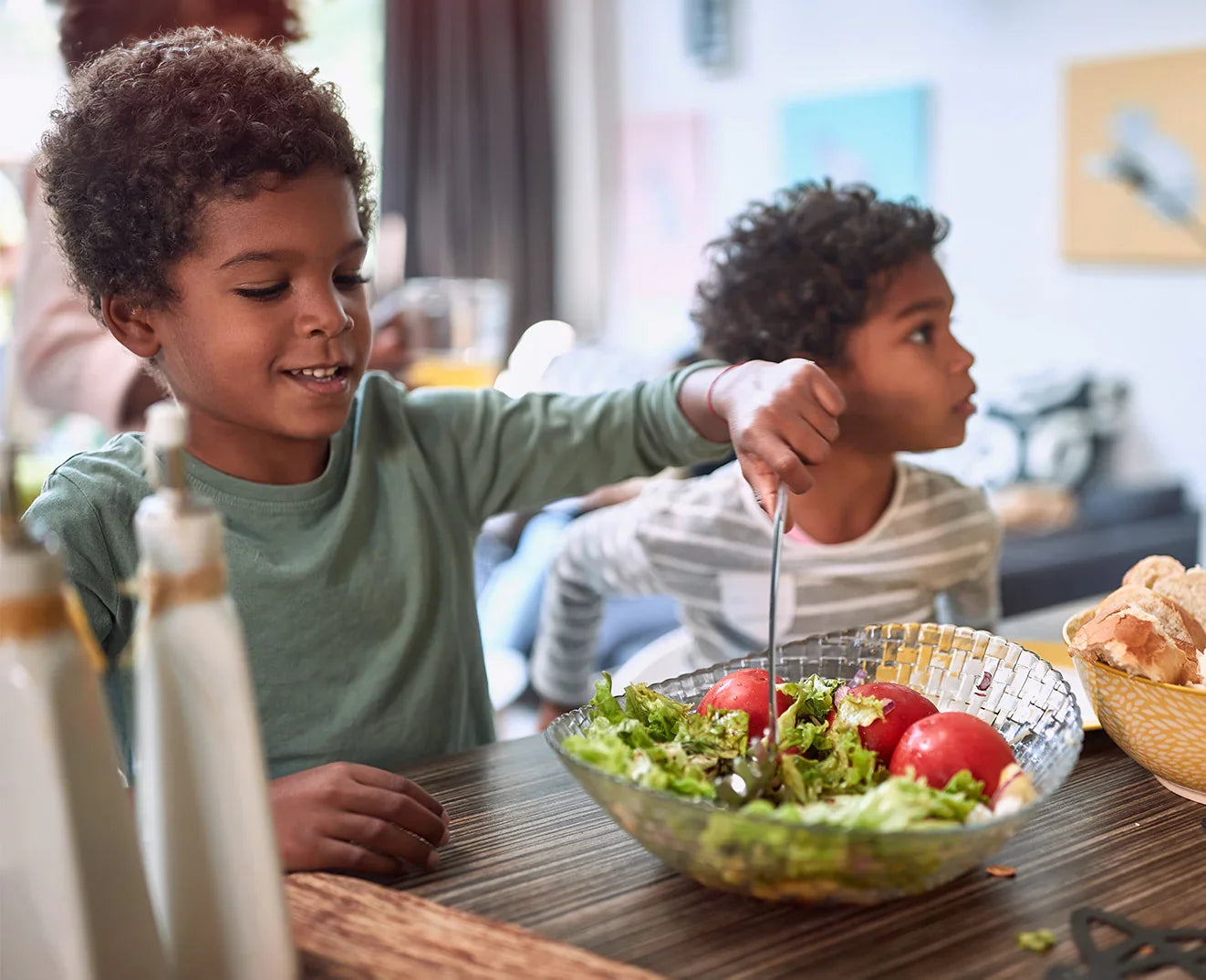 Two children at a dining table with a salad and bread basket.